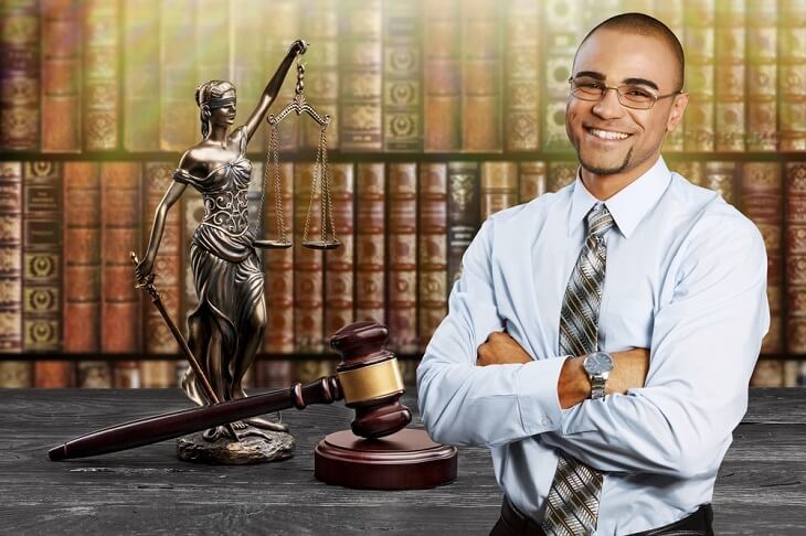 A young African American legal assistant with law books smiling and behind him law books.